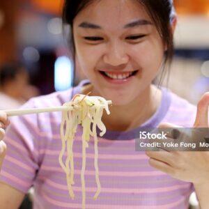 An Asian young woman is enjoying a bowl of Malaysian asam laksa (spicy fish broth noodle) in restaurant