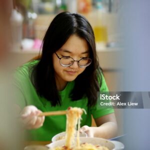 A teenage girl is enjoying mealtime while using smartphone for online learning during lockdown in Malaysia.