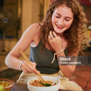 Shot of a young woman eating a bowl of prawn noodle soup in a Vietnamese restaurant